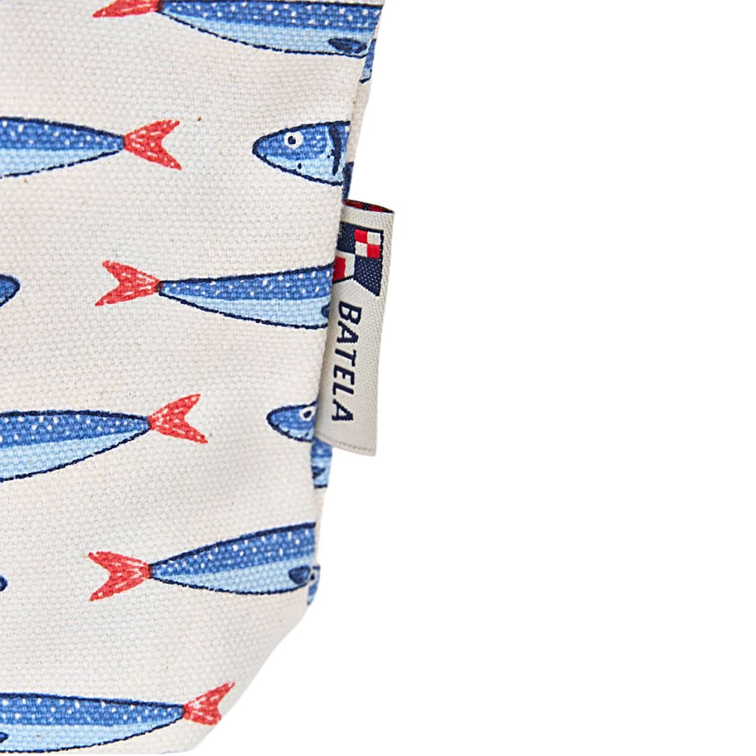 Los pequeños detalles también pueden transmitir un estilo propio. Este neceser de algodón con estampado de peces Batela refleja perfectamente el carácter marinero que identifica a la marca, combinando funcionalidad y diseño inspirado en el mar.  Está confeccionado en algodón resistente, un material ligero y agradable al tacto que resulta muy práctico para el uso diario. Su estampado repetido de peces en tonos azules con detalles en rojo sobre fondo claro aporta un aire fresco y dinámico que recuerda a la vida marina.  El neceser cuenta con cierre superior mediante cremallera, lo que permite guardar de forma segura todo lo que necesites llevar contigo. Su formato compacto facilita transportarlo dentro de un bolso, mochila o maleta sin ocupar demasiado espacio.  Por su tamaño es perfecto para guardar maquillaje, productos de higiene, accesorios pequeños o cualquier objeto que quieras mantener organizado tanto en el día a día como durante viajes o escapadas.  El diseño encaja especialmente bien con el estilo marinero y náutico característico de Batela, por lo que combina fácilmente con otros complementos de la marca o con accesorios inspirados en el mundo del mar.  Un accesorio práctico, ligero y con personalidad, ideal para quienes disfrutan de los detalles con inspiración marina.